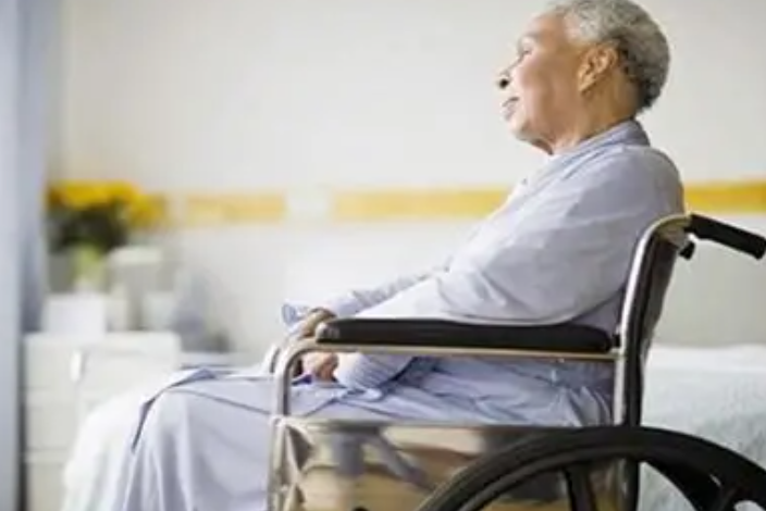 An elderly person sits on a chair with a donut pillow