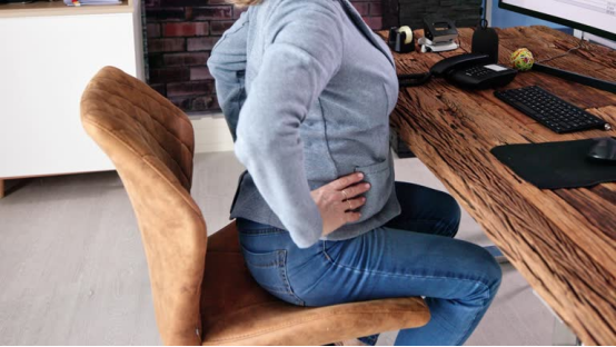 Office worker with back pain, illustrating how a donut pillow can address discomfort in global sitting culture.