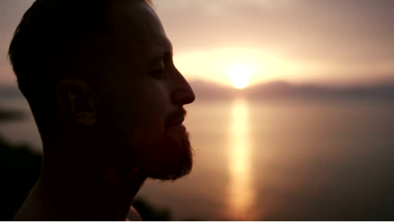 Man meditating by the sea at sunset, a serene setting where a donut pillow could enhance comfort during mindfulness practice