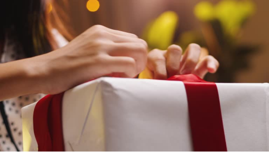 Hands tying a red ribbon on a white gift box, representing the bamboo charcoal donut pillow as a thoughtful, health-focused present for family.